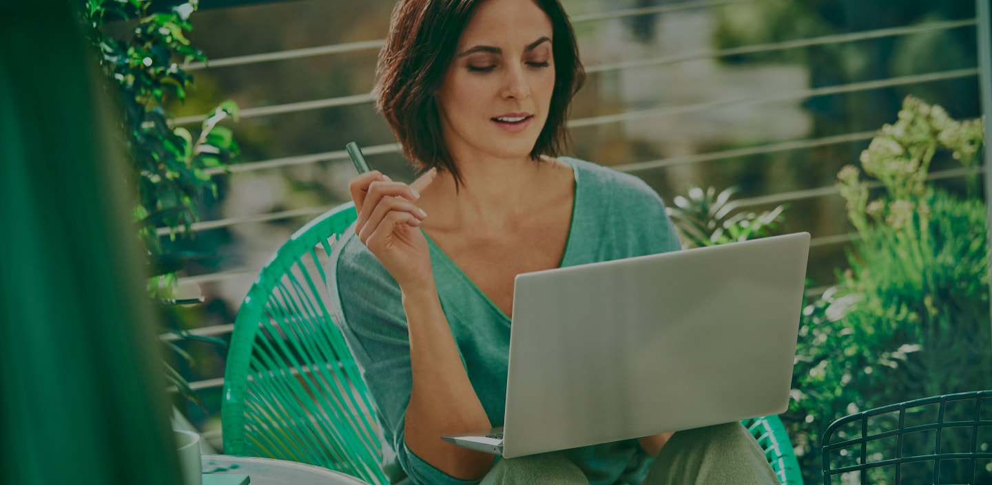 A woman holds an IQOS device while looking at a laptop.